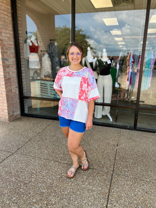 Woman wearing colorful patchwork top with floral and geometric patterns standing outside clothing boutique
