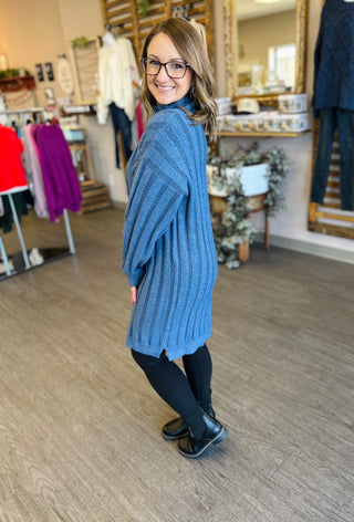 Woman wearing blue ribbed knit sweater dress with mock neck in boutique clothing store setting.