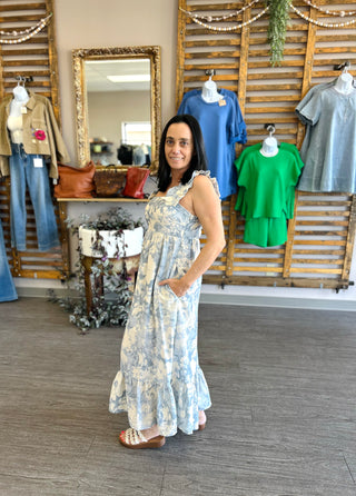 Woman modeling a floral maxi dress in a boutique clothing store setting.
