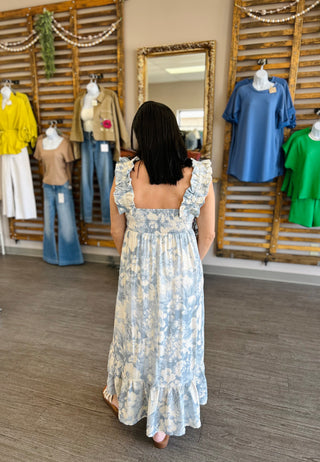 Woman wearing floral maxi dress with ruffled straps shopping in boutique store with clothing displays