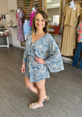 Woman wearing blue feather-print romper with bell sleeves in clothing boutique setting