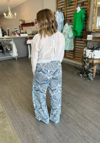 Woman wearing white blouse and blue floral print wide-leg pants in clothing boutique store