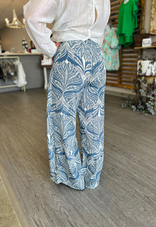 Person wearing wide-leg wrap pants with blue and white tropical leaf pattern in clothing store