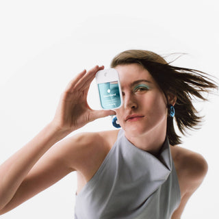 Woman holding Touchland hand sanitizer bottle up to her eye with hair flowing in motion.