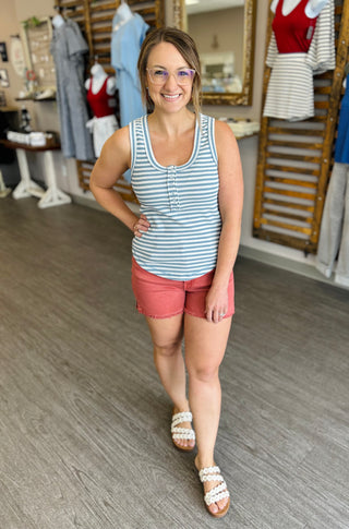 Woman wearing coral-colored frayed hem shorts with striped tank top in clothing boutique store.