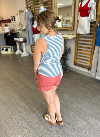 Woman wearing blue and white striped sleeveless tank top with coral shorts in clothing store