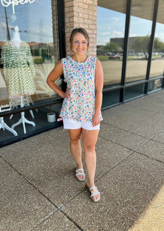 Woman wearing floral sleeveless tank top with white shorts standing outside boutique storefront