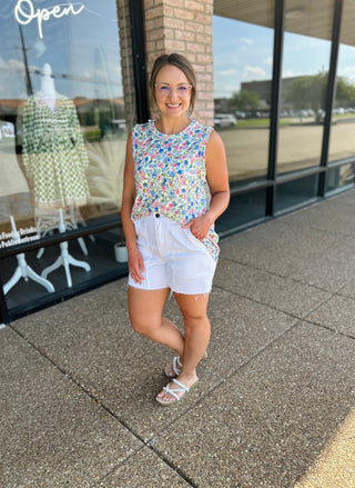 Woman wearing floral sleeveless tank top with white denim shorts standing outside boutique storefront
