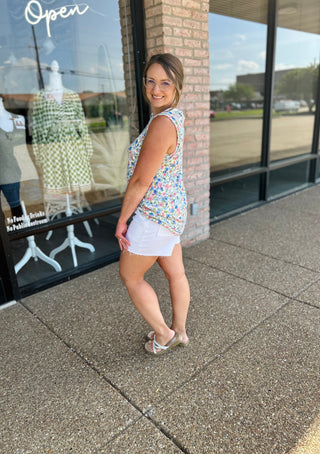 Woman wearing floral sleeveless tank top and white denim shorts standing outside boutique storefront