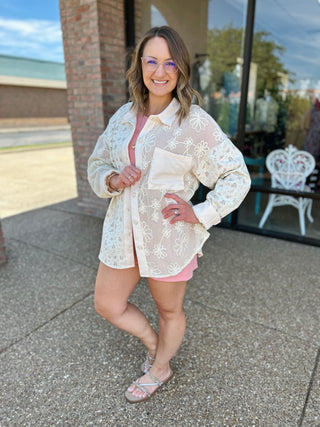 Woman wearing white lace patchwork button-down top over pink outfit, posing outdoors with confident smile.