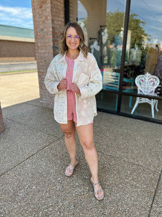 Woman wearing white floral patchwork button-down top over pink outfit, standing outside storefront