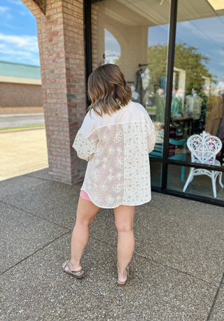 Woman wearing white lace patchwork button-down top walking on sidewalk in front of storefront.