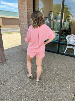 Woman wearing pink casual short set standing outside storefront, viewed from behind