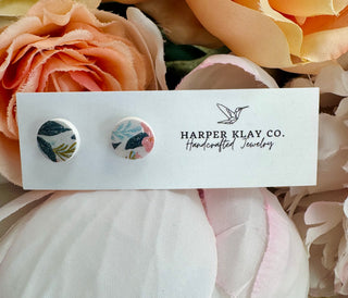 Handcrafted floral stud earrings on white display card surrounded by peach silk flowers and ribbons.