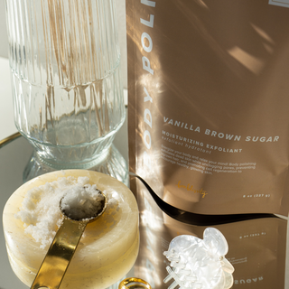 Bonblissity vanilla brown sugar body polish scrub package with glass vase and golden spoon in sunlit setting