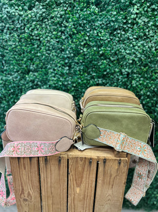Boho crossbody bags with decorative guitar straps displayed on wooden surface against green foliage background.
