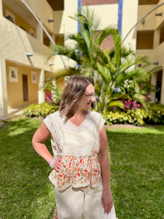 Woman wearing white boho paisley top with lace trim and floral belt in tropical courtyard setting.