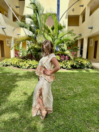 Woman wearing boho paisley sleeveless top standing in tropical courtyard with palm trees and landscaping.