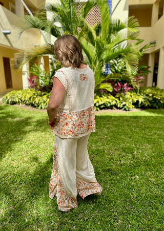 Woman wearing floral paisley boho top and matching pants standing on grass in tropical setting.