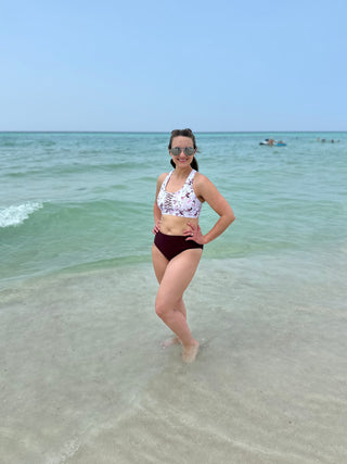 Woman wearing floral bikini top and dark swim bottoms standing in shallow ocean water at beach