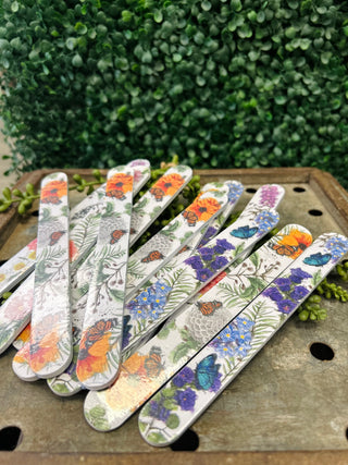 Decorative nail files with colorful butterfly and floral patterns arranged on wooden surface outdoors