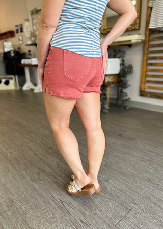 Woman wearing coral frayed hem denim shorts with striped top and sandals in kitchen setting