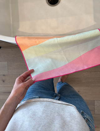 Person holding colorful striped kitchen towel with gradient design near white bathtub in bathroom setting.