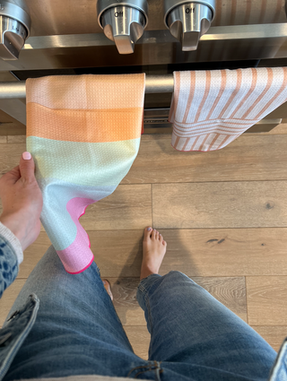 Person holding colorful striped kitchen towel near stainless steel stove with matching towel hanging from handle.