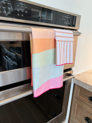 Colorful striped kitchen towels hanging on stainless steel oven handle in modern kitchen.