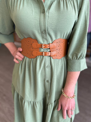 Woman wearing sage green dress with brown perforated leather stretch belt featuring dual buckles