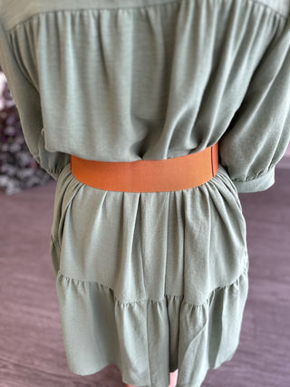 Woman wearing sage green dress with orange perforated stretch belt cinched at waist