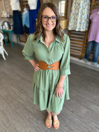 Woman wearing sage green dress with brown perforated stretch belt in clothing boutique