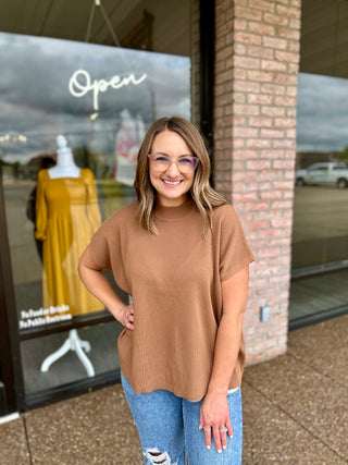 Woman smiling outside boutique wearing a ribbed short-sleeve mock neck sweater top with jeans.