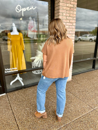 Woman wearing a ribbed short-sleeve relaxed sweater top paired with cuffed jeans and clogs.