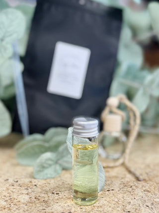 Small glass bottle of car freshener oil with cork stopper on natural surface with greenery background.