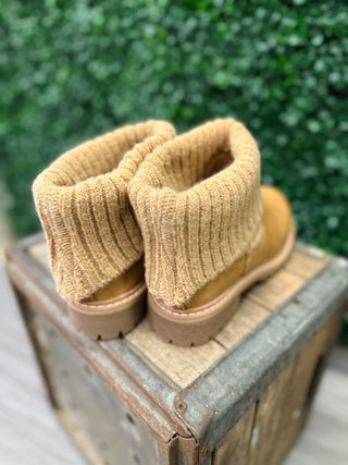 Caramel-colored ankle boots with knit sweater cuffs and brown soles displayed on wooden crate outdoors.