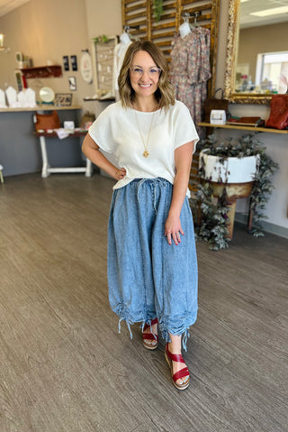 Woman wearing white top and chambray wide leg pants with cinched hem details in boutique setting