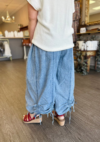 Woman wearing loose-fitting wide leg chambray pants with cinched hem details and frayed edges.
