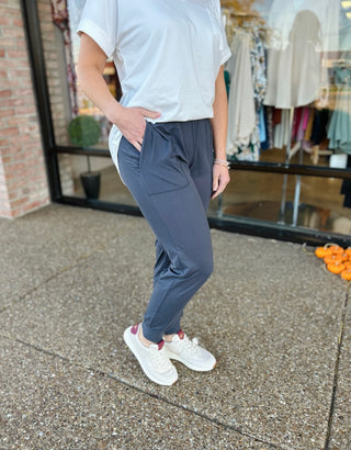 Person wearing charcoal joggers with white sneakers standing on concrete sidewalk outside retail store
