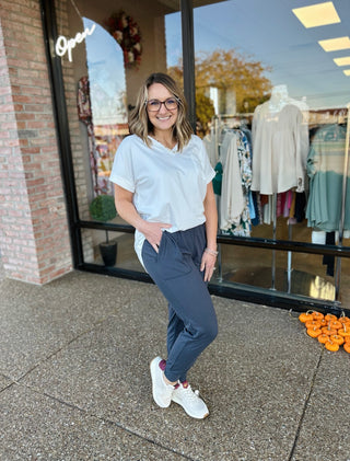 Woman wearing white t-shirt and charcoal joggers standing outside clothing boutique storefront