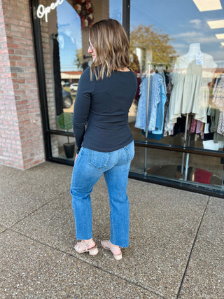 Woman wearing charcoal ribbed square neck long sleeve top with blue jeans standing outside boutique storefront.