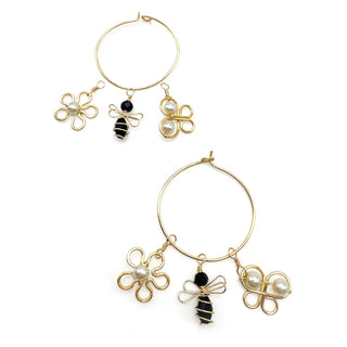 Gold hoop earrings with flower, bee, and clover charms featuring pearl and black accents.