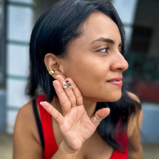 Woman wearing ornate gold statement earrings with colorful gemstones, touching her ear gently.