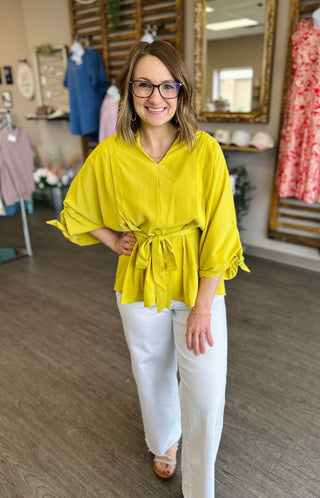 Woman wearing yellow belted blouse with white pants standing in clothing boutique interior