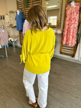 Woman wearing bright yellow long-sleeved top with white pants in clothing boutique store