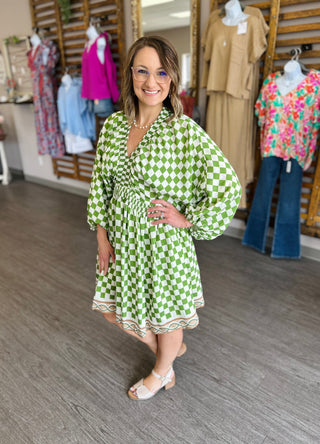 Woman wearing green and white checkered dress with long sleeves in boutique clothing store setting.