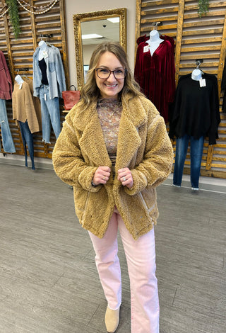 Woman wearing cozy textured jacket in clothing boutique with vintage mirror and hanging garments