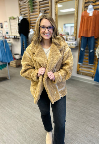 Woman wearing cozy textured jacket in clothing store, smiling at camera while trying on outerwear.