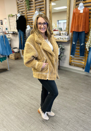 Woman wearing cozy sherpa jacket in clothing store, smiling at camera with casual outfit.