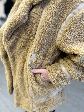 Person wearing cozy sherpa fleece jacket with thumb through sleeve opening, showing soft textured fabric.